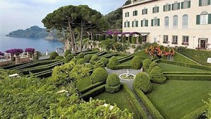 Un jardin à la française, avec des haies taillées avec soin et un grand bâtiment doté de nombreuses fenêtres.