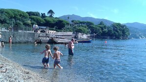Une plage avec une eau claire, des galets et des gens.