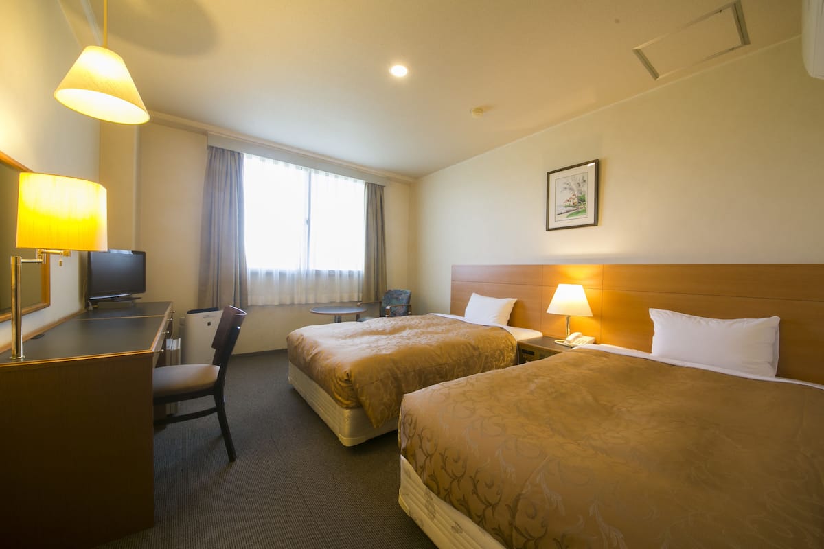 A hotel room with two beds, a desk, a chair, a television, and a window with curtains.