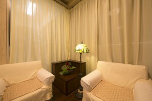 Une pièce comprenant deux fauteuils blancs, une table d’appoint en bois ornée d’un arrangement floral et un lampadaire.