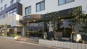 A modern hotel with a glass facade, a curved entrance, and a landscaped garden with rocks and plants.