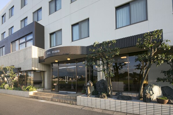 A modern hotel with a glass facade, a curved entrance, and a landscaped garden with rocks and plants.