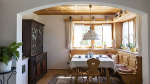 A dining area with a wooden table, chairs, and a window with curtains. - Apartment "Glonntal" between city, lakes & mountains (Glonn)