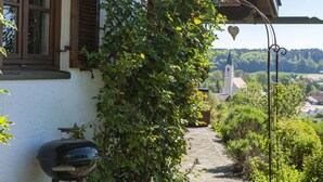 A house with a garden, a barbecue grill, and a view of a church in the distance. - Apartment "Glonntal" between city, lakes & mountains (Glonn)