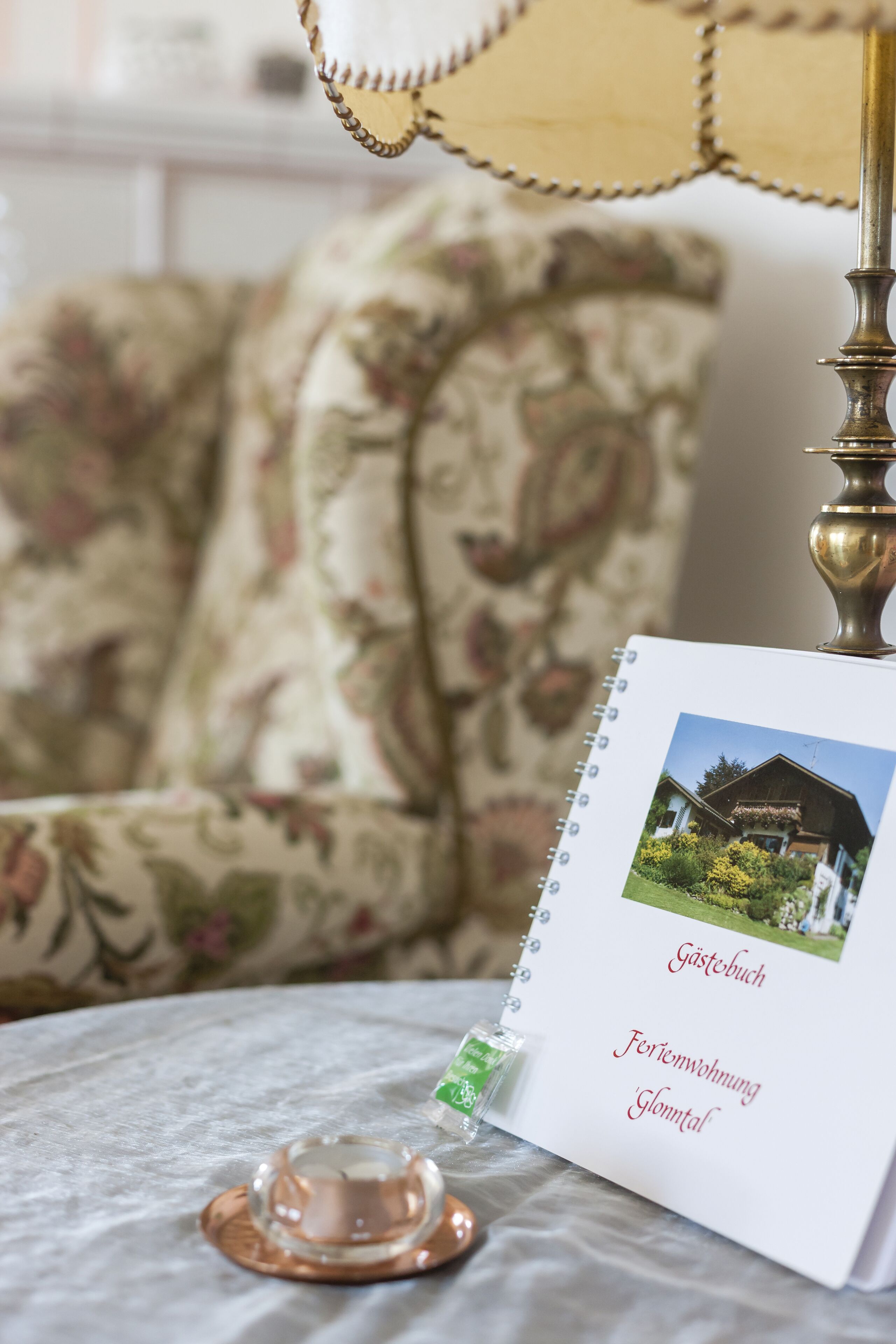 A notebook with a photograph of a house and text in German, placed on a table with a lamp and a candle.