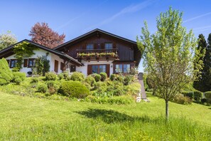 Eine zweistöckige Chalet mit Balkon, umgeben von einem gepflegten Garten und blauem Himmel.