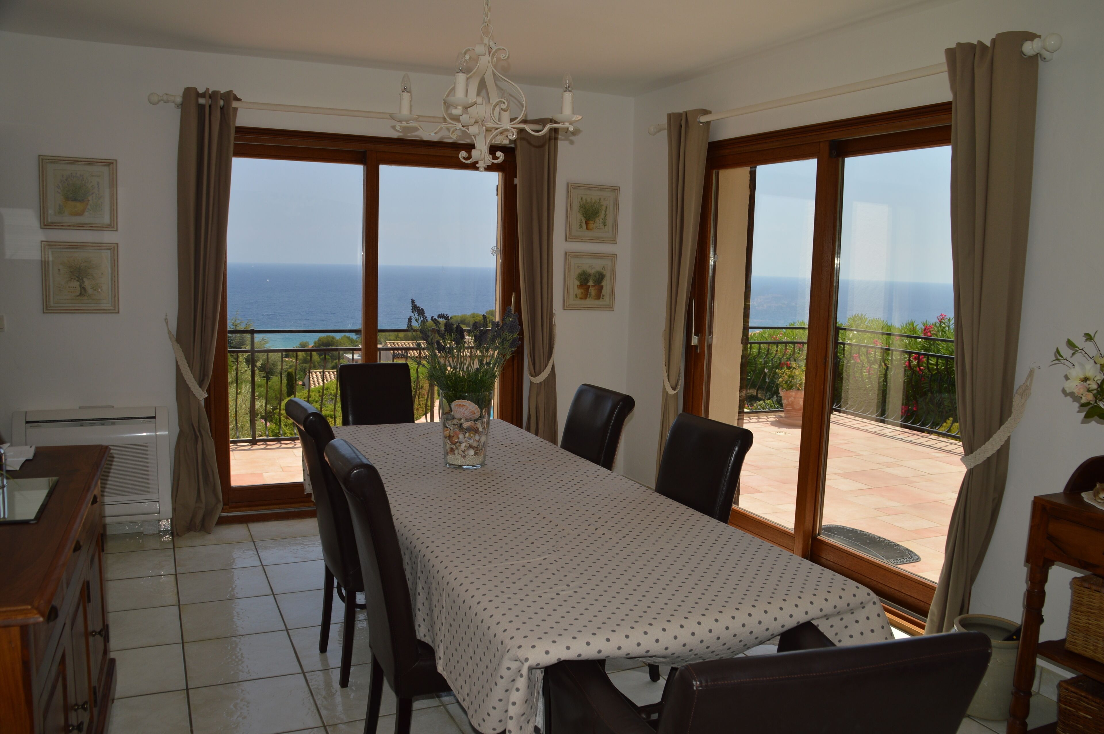 Comedor con una mesa preparada para cuatro, grandes puertas correderas de vidrio que dan a un balcón con vistas al mar.