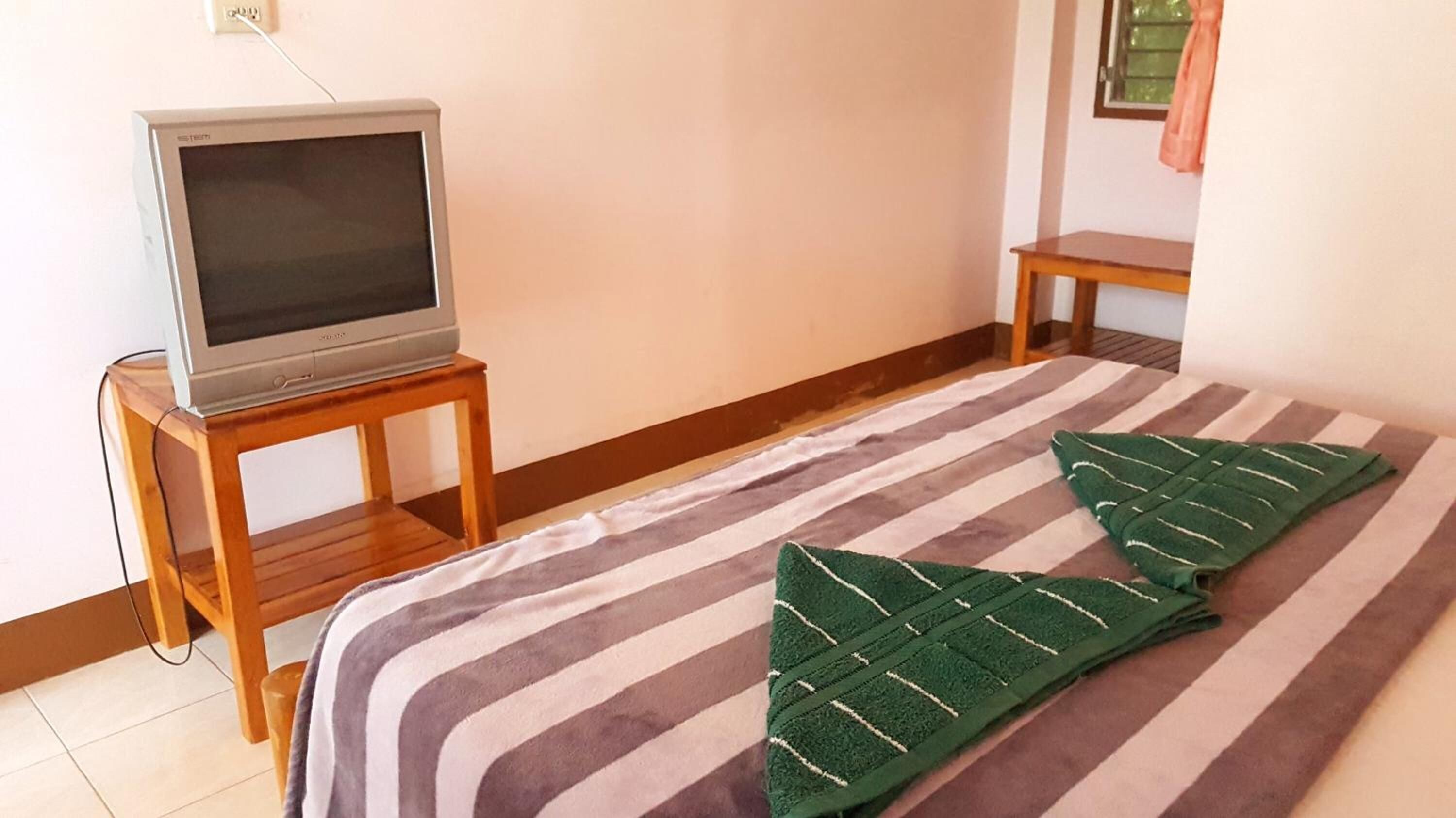 Een kamer met een bed, een televisie op een houten standaard en een raam met gordijn.