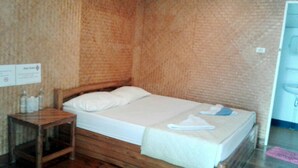 A single bed with a wooden frame, a white mattress, and a matching pillow. There is a wooden nightstand beside the bed with a bottle of water and a tissue box. A towel is placed on the bed.