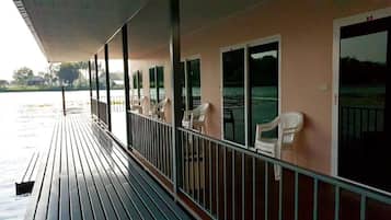 A covered deck with chairs and a railing overlooking a body of water.