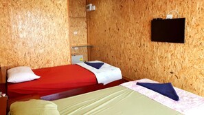 Ein Zimmer mit zwei Betten, Holzwänden, einer kleinen Ablage und einem an der Wand befestigten Fernseher.