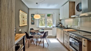 A modern kitchen with a dining area, featuring a large window, stainless steel appliances, and a pendant light.