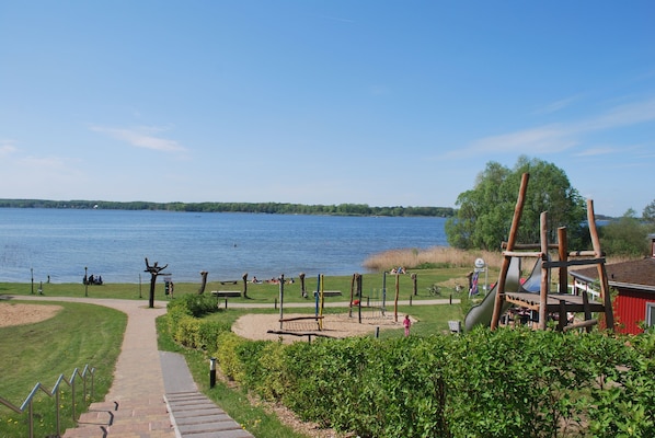 Un parque junto al lago con un parque infantil, senderos para caminar y bancos.
