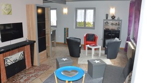 A modern living room with a fireplace, a TV, and a dining area with a table and chairs. - Center Alsace, house 2 to 5 pers. Between Colmar and Strasbourg. Exceptional view (Neubois)