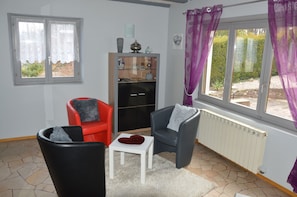 Un salon avec deux fauteuils, une petite table, un meuble et une fenêtre avec des rideaux.