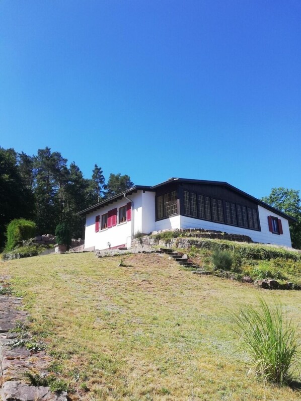 A white building with a dark roof, red shutters, and a stone staircase leading up to it.