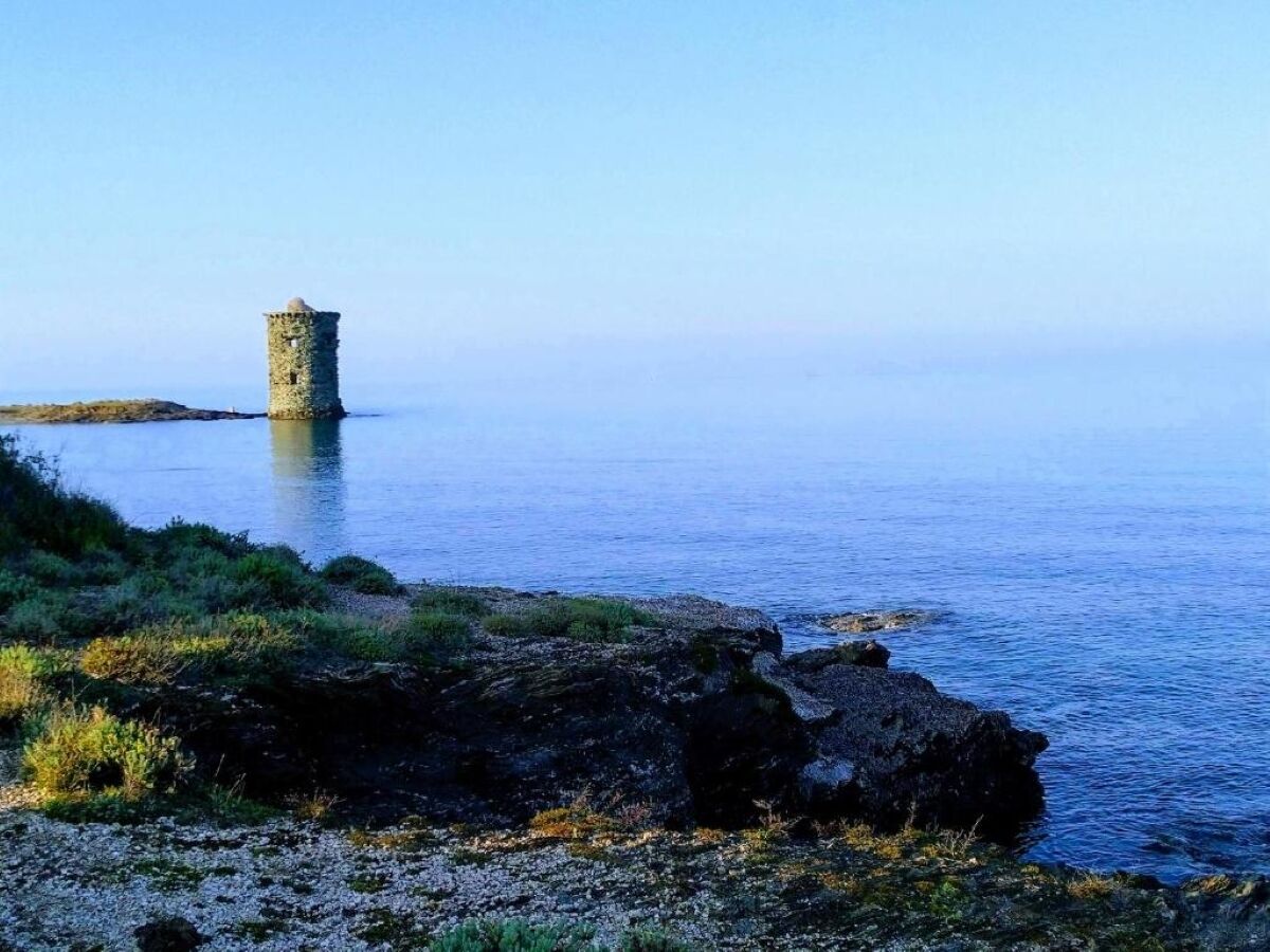 A coastal scene with a stone tower on a small island, surrounded by calm water and rocky shoreline.