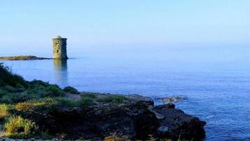 A coastal scene with a stone tower on a small island, surrounded by calm water and rocky shoreline.