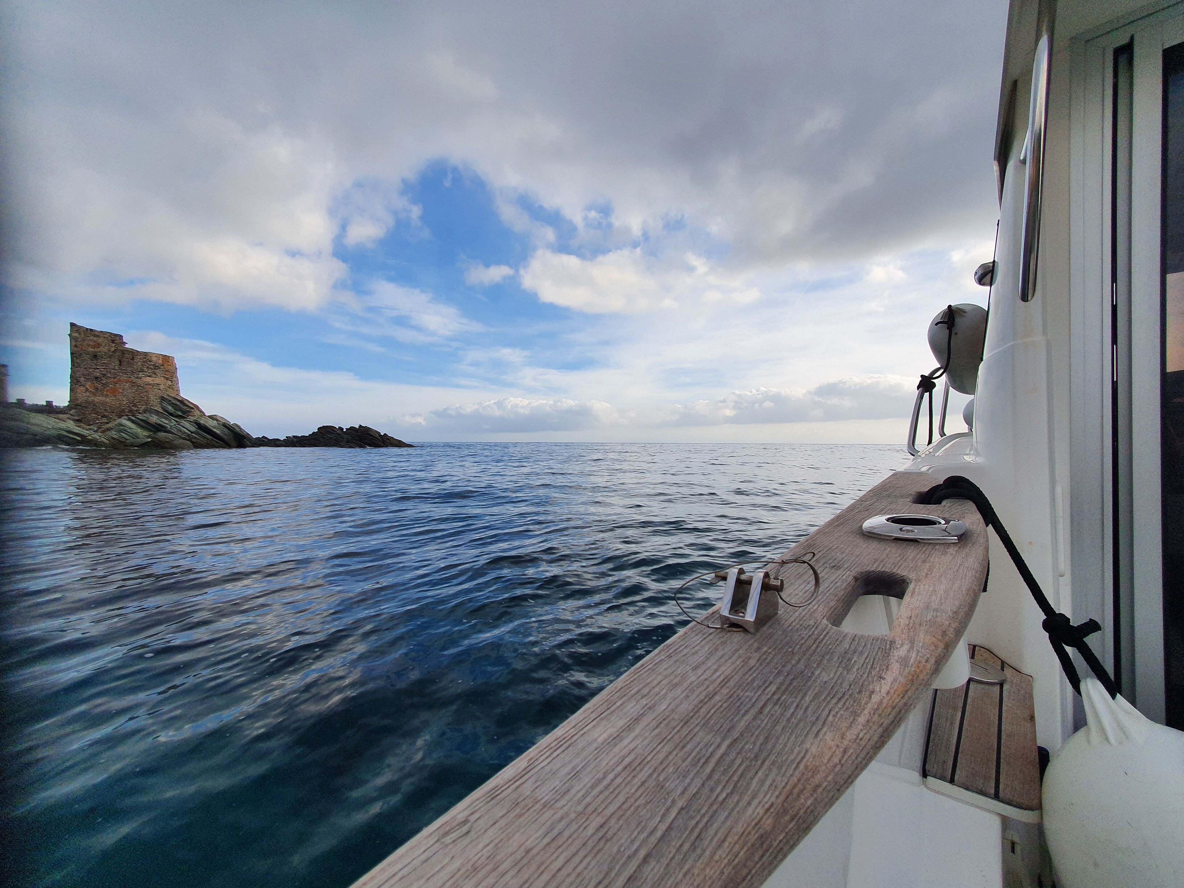A boat's deck with a view of a rocky coastline and a castle-like structure in the distance.