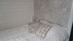 A single bed with a white mattress and a patterned pillow, set against a wall with a textured finish.