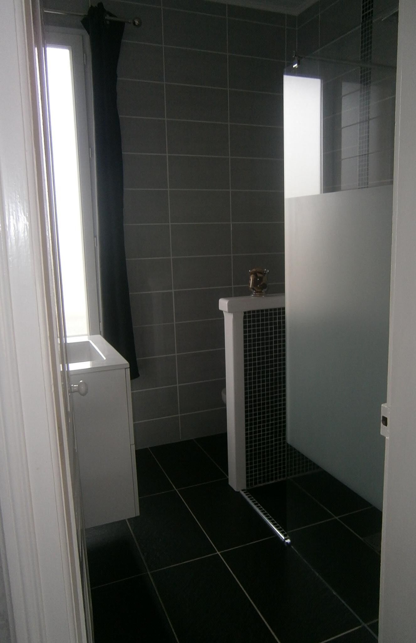 Een kleine, afgesloten badkamer met een douchegedeelte, een toilet en een raam met gordijn.
