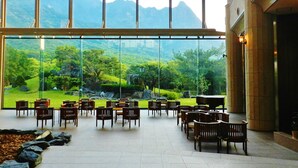 A spacious indoor area with a large window offering a view of a lush green landscape and mountains. - Yakushima Iwasaki Hotel (Yakushima)