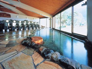 Un spa con suelo de piedra, bañera de hidromasaje y amplias ventanas.