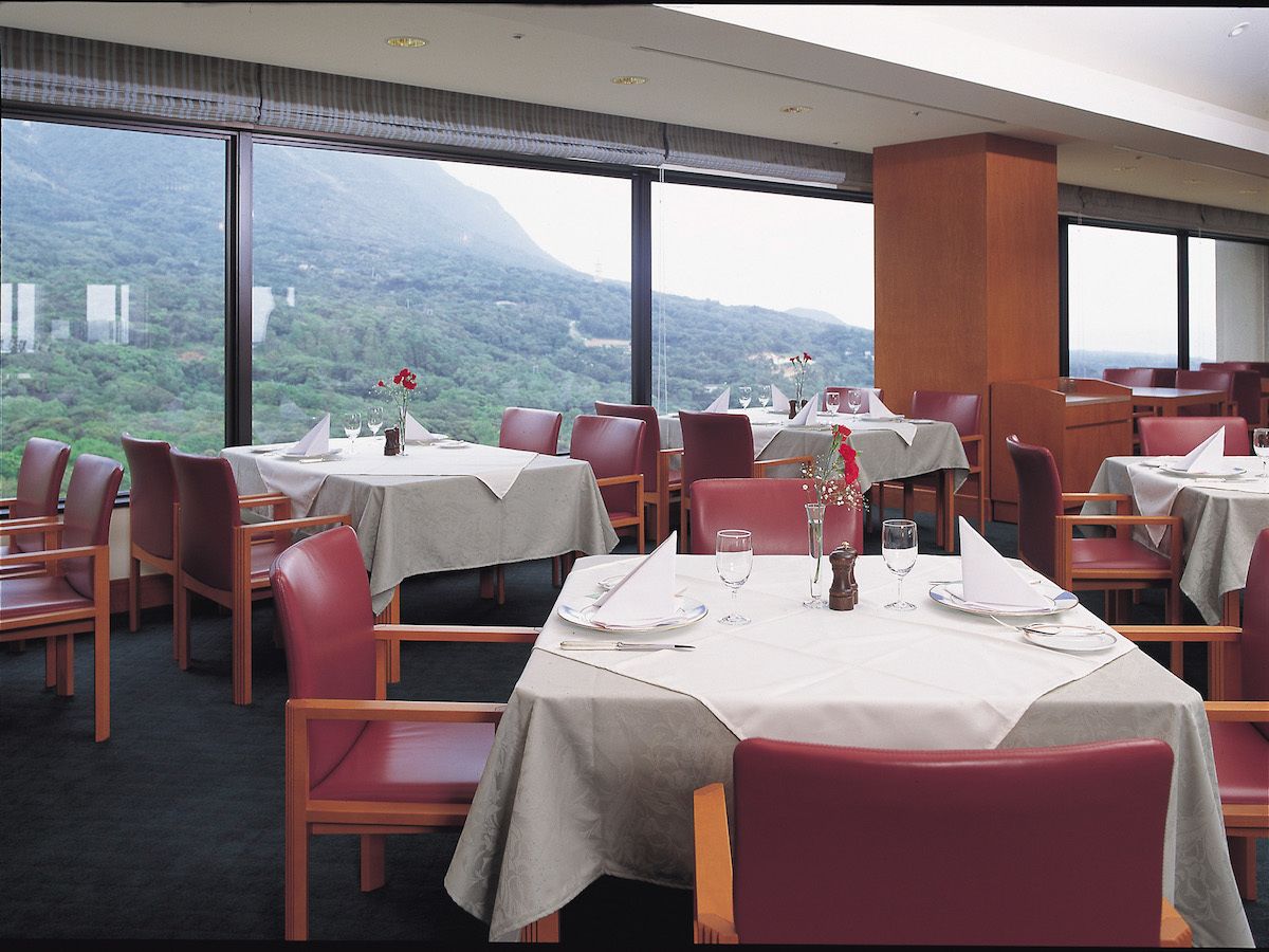 A dining area with tables set for four, large windows offering a view of a mountainous landscape.