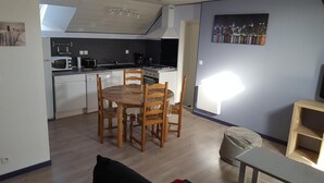 Une cuisine compacte dotée d’appareils électroménagers modernes, un coin repas avec une table ronde et des chaises, et un tableau représentant un paysage urbain accroché au mur.