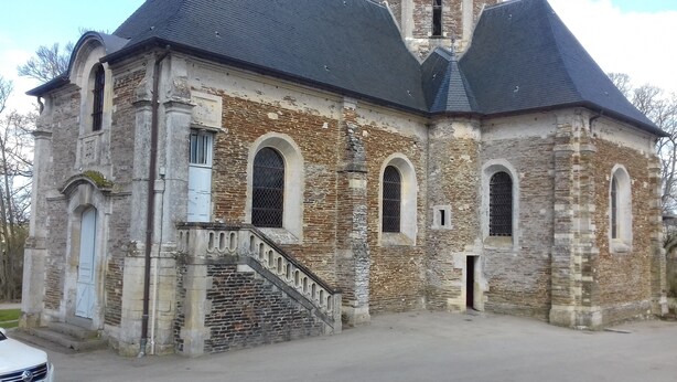 Un bâtiment historique en pierre, doté d’un toit à forte pente, de fenêtres en arc de cercle et d’un petit escalier menant à l’entrée.
