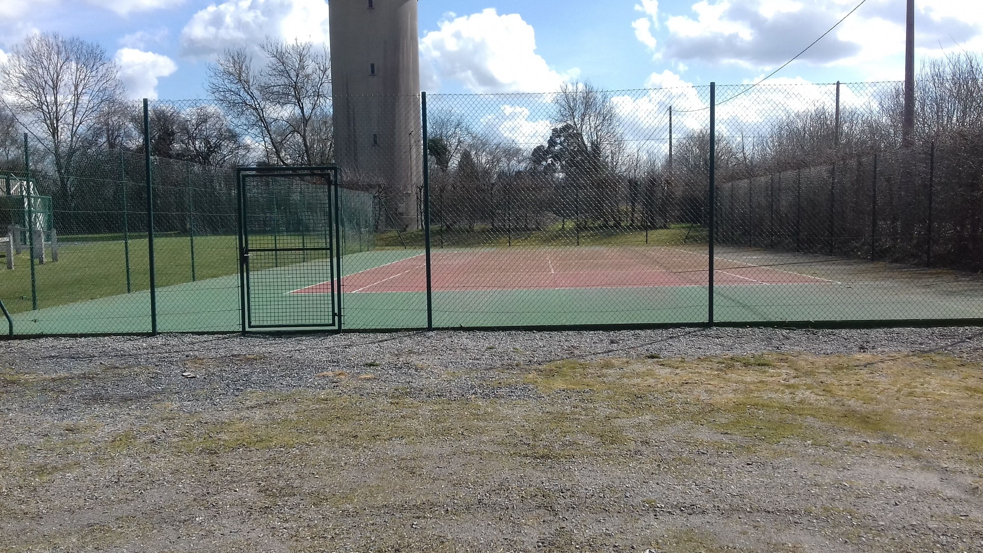 Una cancha de tenis cercada con un sendero de grava frente a ella.
