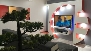 A modern living room with a flat-screen TV mounted on a wall, surrounded by recessed lighting. There are two grey sofas and a small table with a red accent. - Maginifique T2 seasonal rental (SAINT ESPRIT)