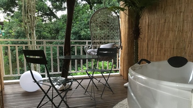 A wooden deck with a hot tub, two foldable chairs, and a wicker chair. - Maginifique T2 seasonal rental (SAINT ESPRIT)