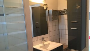 A modern bathroom with a white sink, dark cabinets, and a mirror. - Maginifique T2 seasonal rental (SAINT ESPRIT)