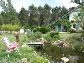 Ein rustikales Haus mit Teich, umgeben von viel Grün und einem Stuhl.