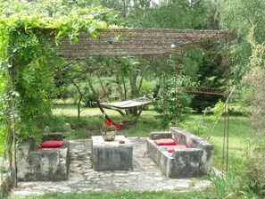 Ein Garten mit einer Hängematte, Betonbänken und einer Pergola.