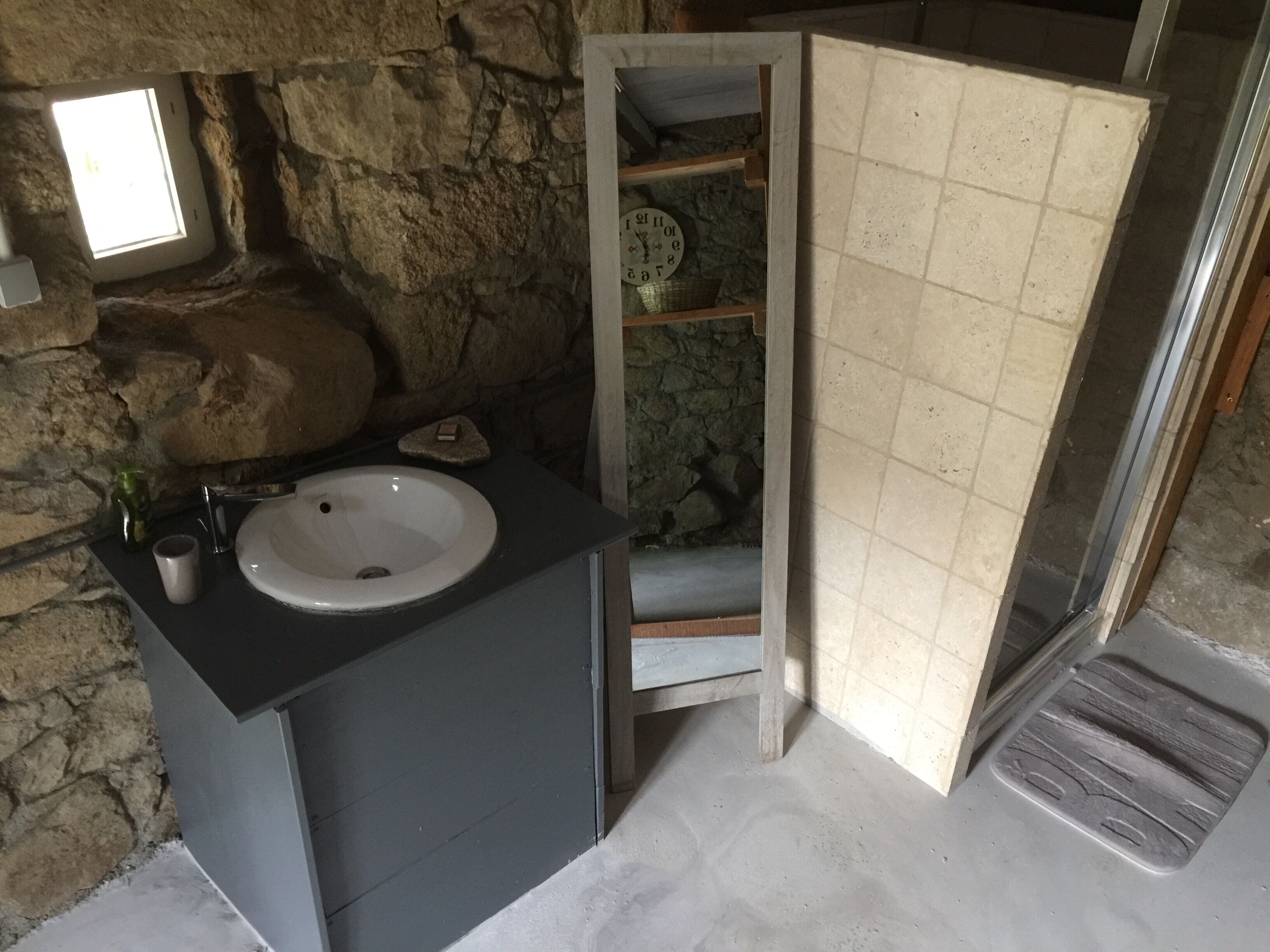A bathroom with a stone wall, a sink, a mirror, and a shower area.