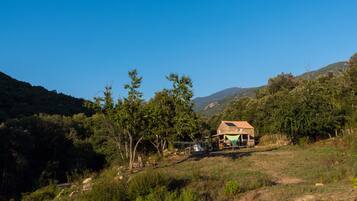 Une maison de campagne avec un toit en pente, entourée d’arbres et de collines.
