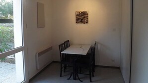 A small dining area with a table and four chairs, a radiator, a framed picture on the wall, and a window providing natural light. - seasonal rental (Vannes)
