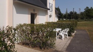 A building with a white exterior, a dark roof, and a small window with a cross symbol. There is a paved path leading to a white table and chair set. - seasonal rental (Vannes)