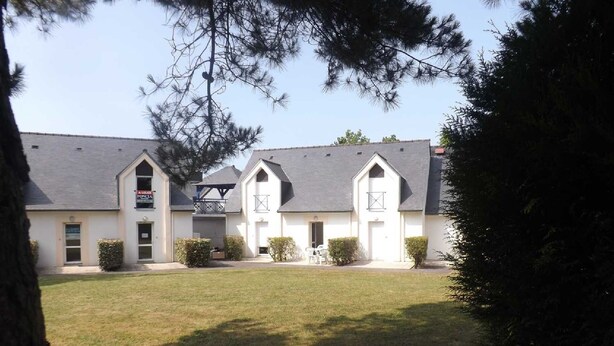 A two-story building with a symmetrical facade, a central entrance with a small porch, and a sign indicating a business or service on the ground floor. - seasonal rental (Vannes)