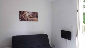 A room with a bed, a flat-screen TV mounted on the wall, and a painting above the bed. - seasonal rental (Vannes)