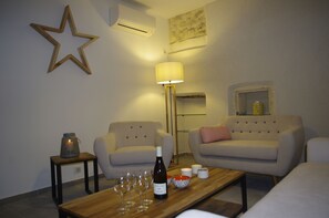 Un salon avec deux canapés, une table basse en bois sur laquelle se trouvent des verres à vin et une bouteille, un lampadaire et une décoration en forme d’étoile accrochée au mur.