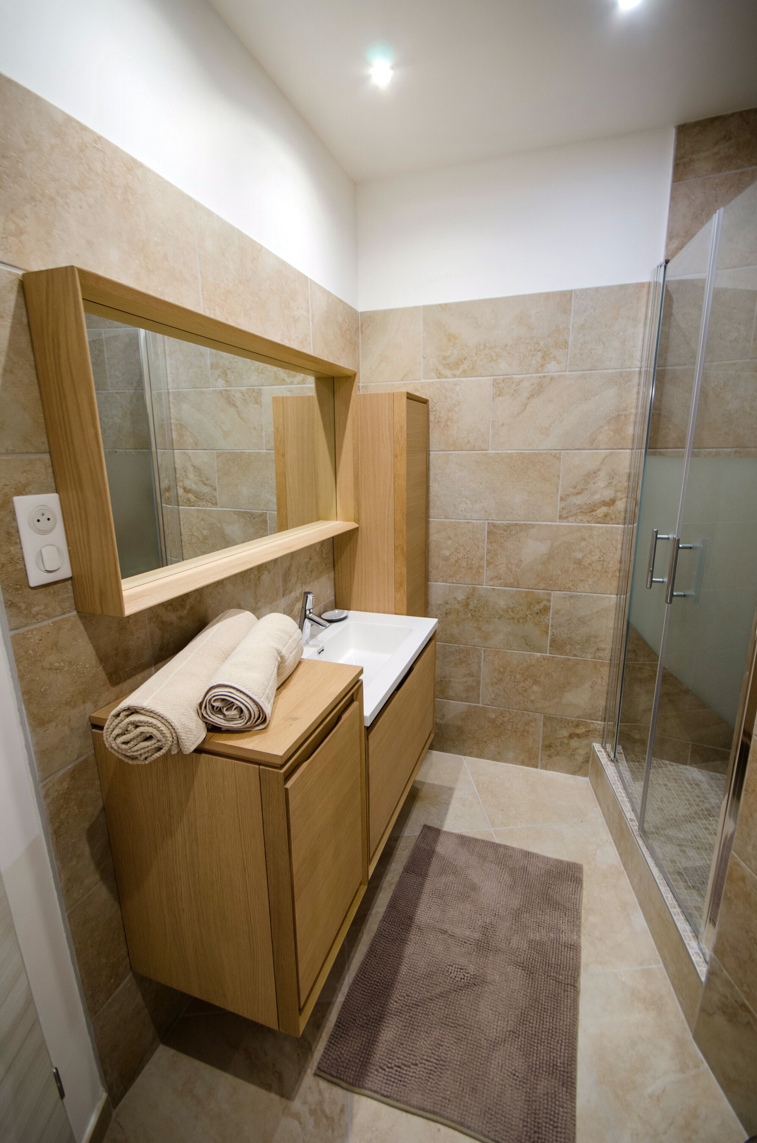 A bathroom with a wooden vanity, a mirror, a sink, and a shower area.