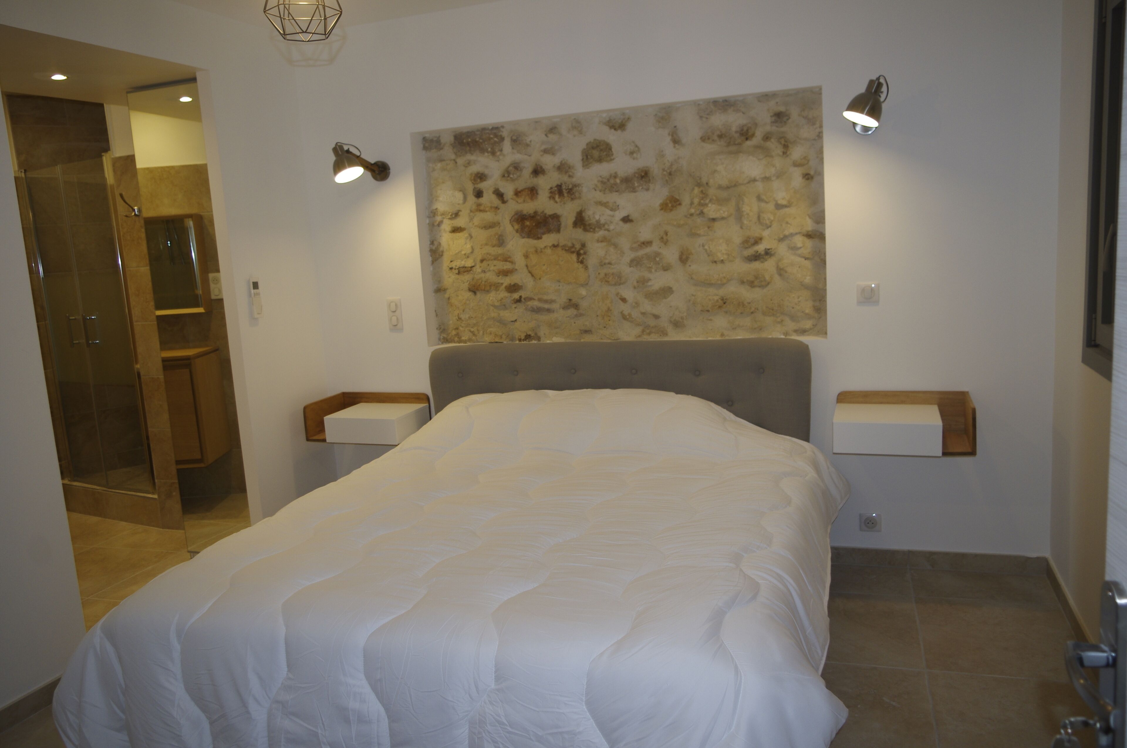 A bedroom with a large bed, a stone wall, and two bedside tables.