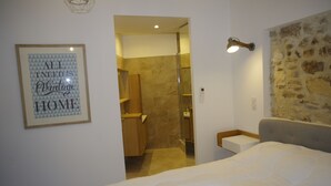 Habitación de hotel con una cama, una cita enmarcada en la pared, ducha y pared de piedra.