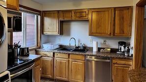A kitchen with wooden cabinets, a stainless steel dishwasher, a microwave, a sink, and a coffee maker. - 1 Block from the Bay!  (Seward)