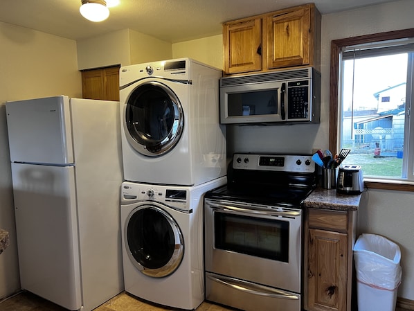 A compact kitchen with a refrigerator, stacked washer and dryer, microwave, oven, and wooden cabinets.