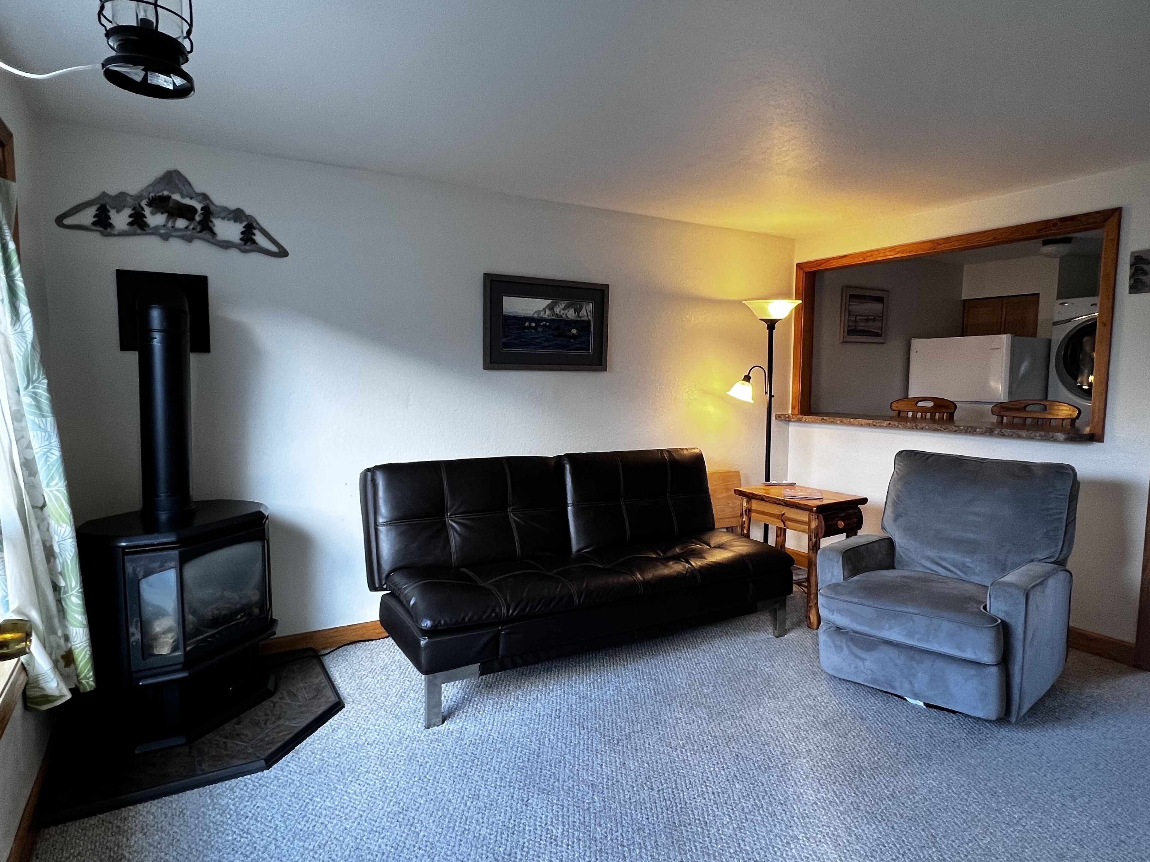 A living room with a black sofa, a grey armchair, a fireplace, a framed picture, and a lamp.