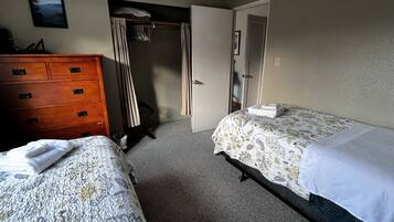 A hotel room with two beds, a wooden dresser, a closet, and a door leading to another room.